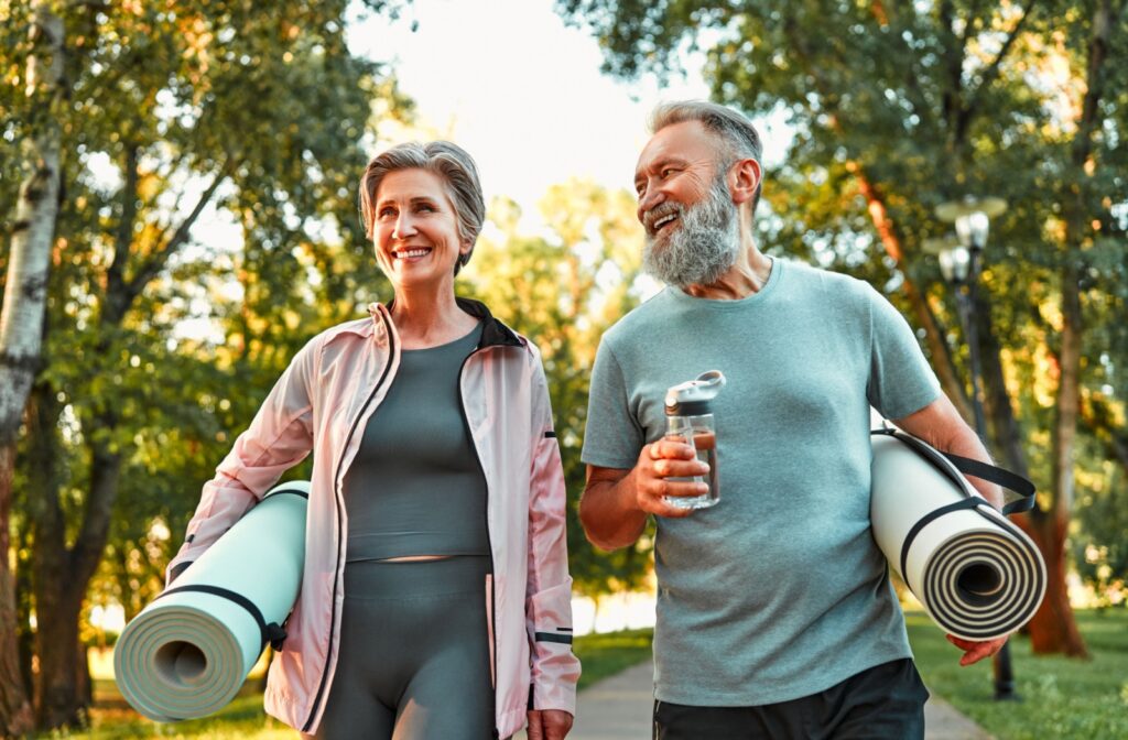 A mature couple enjoying their outdoor walk while holding their yoga mats.
