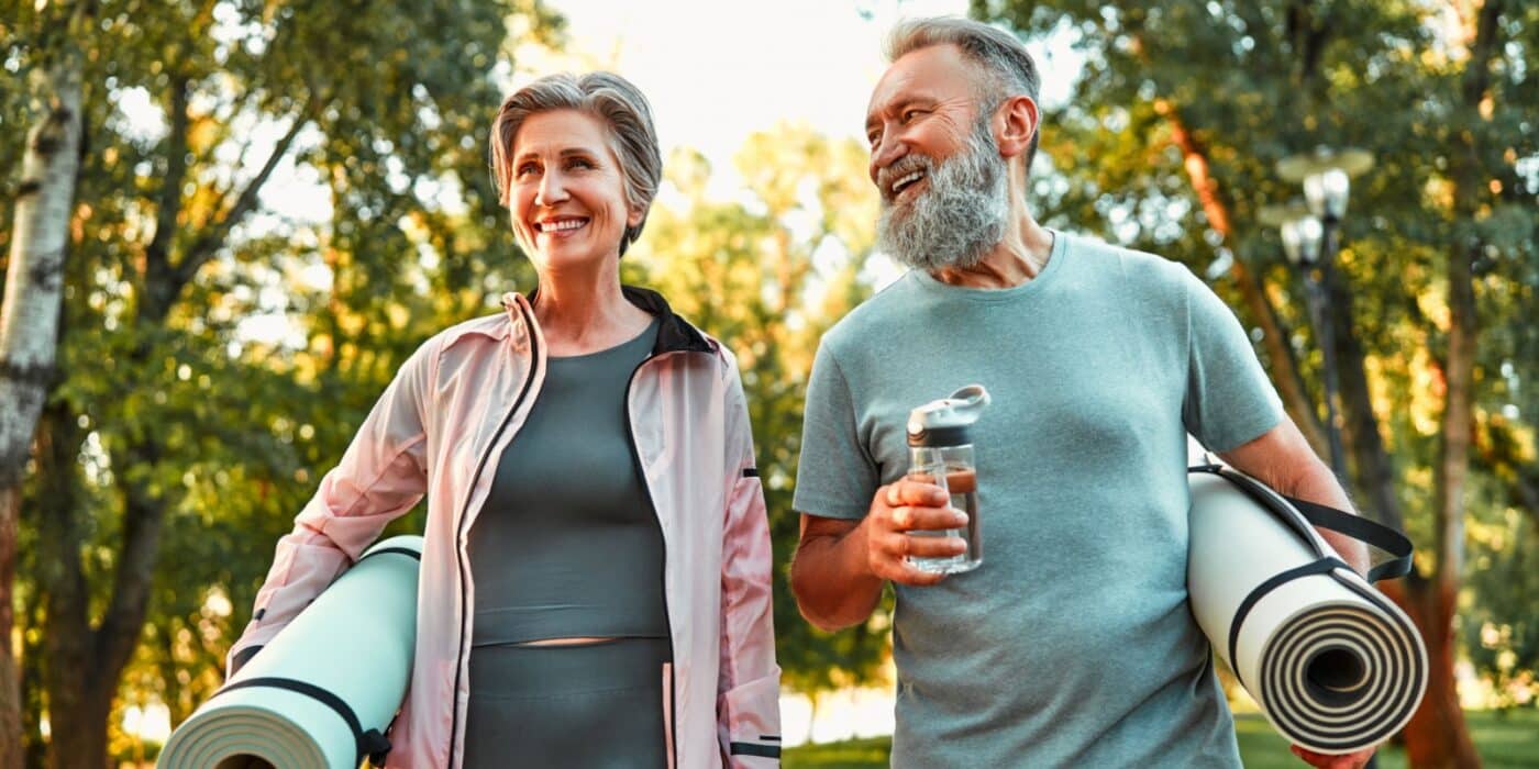 A mature couple enjoying their outdoor walk while holding their yoga mats.