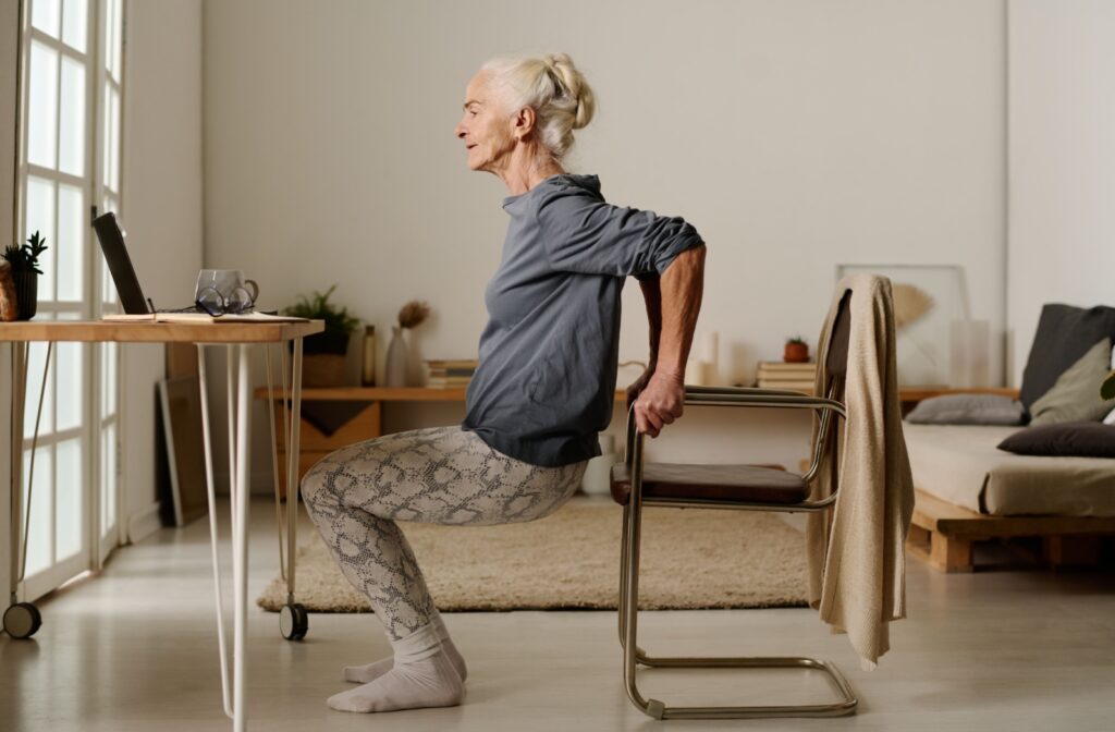 An older adult using their chair for support while doing body weight exercises.