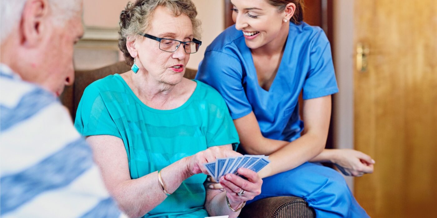 An assisted living caregiver happily supervises senior living residents playing a card game in their assisted living community.