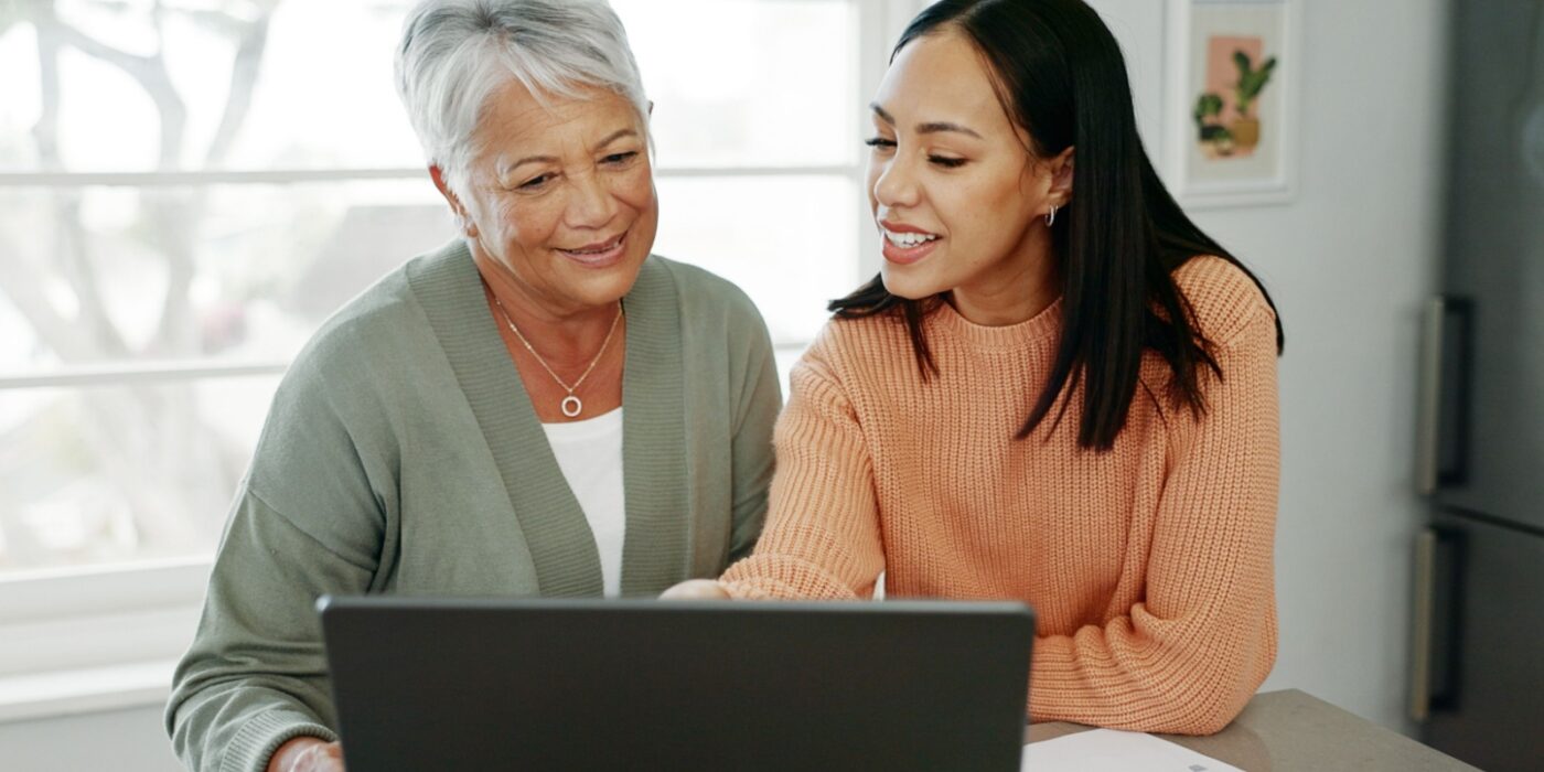 A younger adult helping an older adult use a laptop while discussing care options