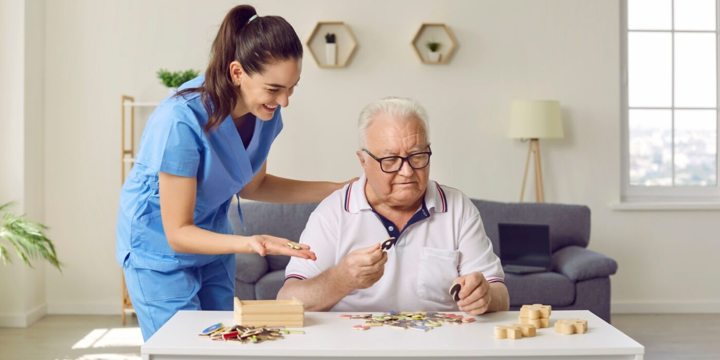 an older person is doing a puzzle that supports memory in their memory care facilitiy with their health care aid.