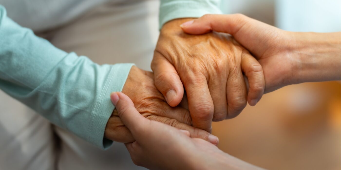 A close-up of an elderly person's hands being held by a younger person