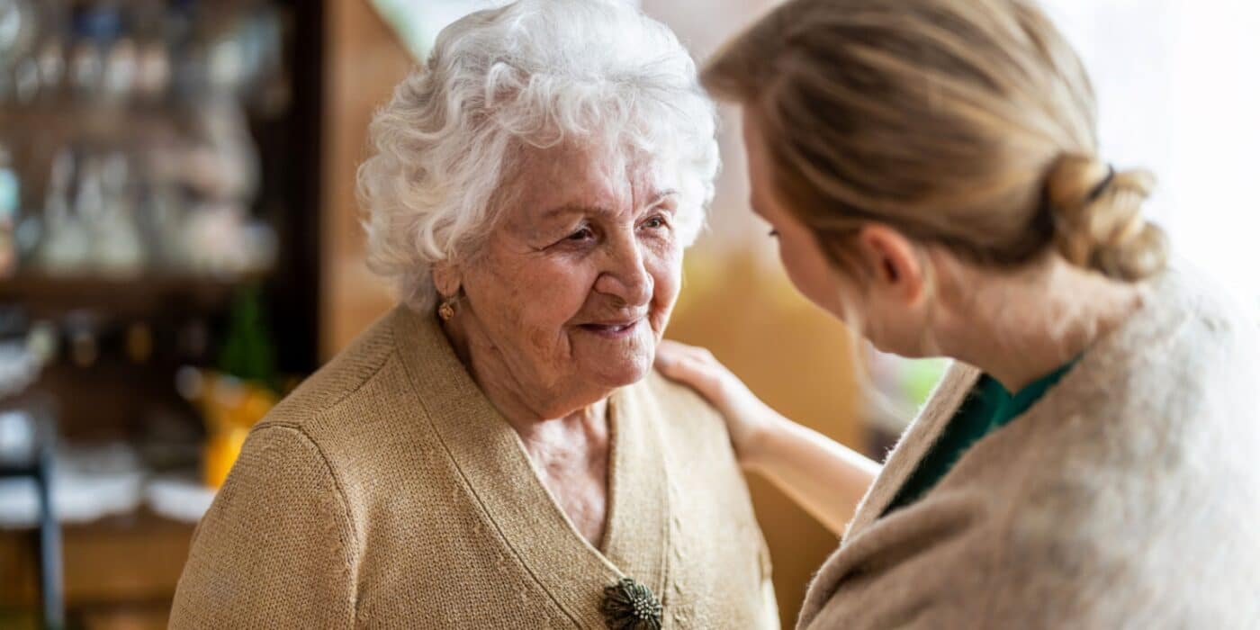 A caregiving staff member talking to an elderly woman with alzheimer's.