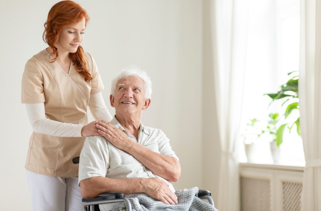 A senior man in a wheelchair being assisted by a caregiver.