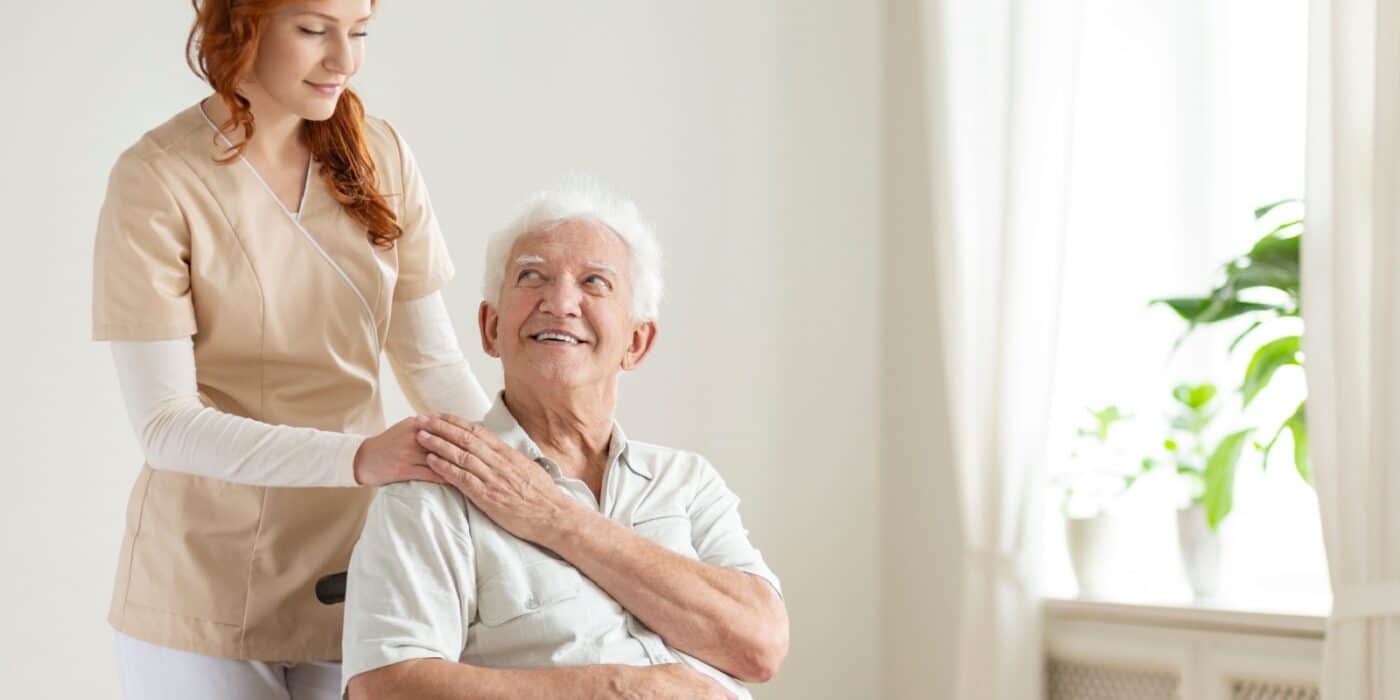 A senior man in a wheelchair being assisted by a caregiver.