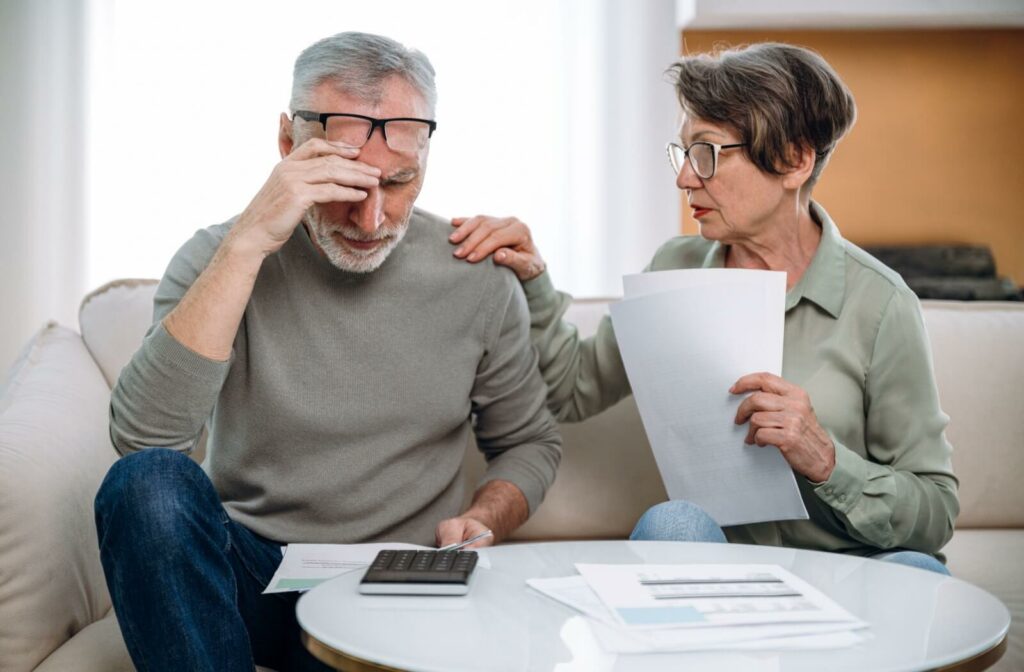 A couple sitting on the couch in worry with the man holding his head.