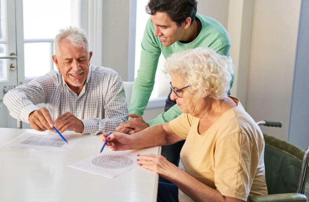 A senior man and woman engaging in a puzzle game with a male caregiver standing beside them.