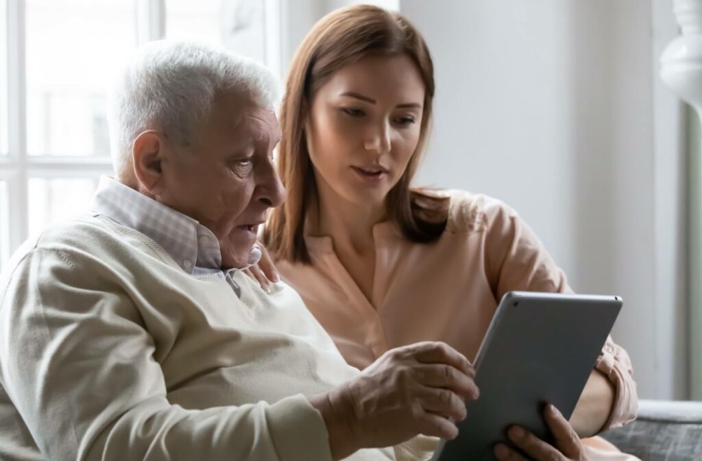 A daughter spending time with her aged father on a couch scrolling through old photos on an ipad.