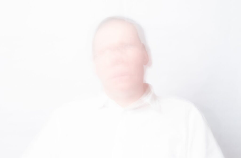 A faded and blurry picture of a senior against a white background symbolizes the depersonalization of hallucinations.