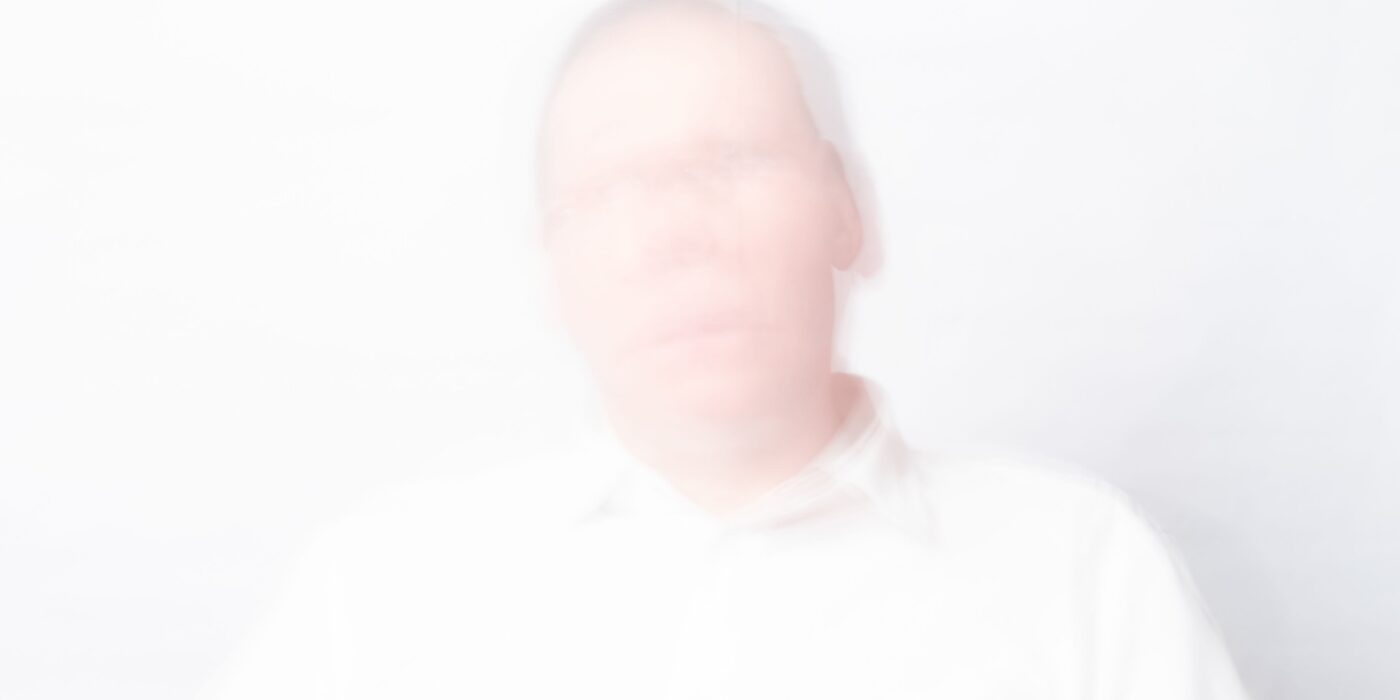 A faded and blurry picture of a senior against a white background symbolizes the depersonalization of hallucinations.