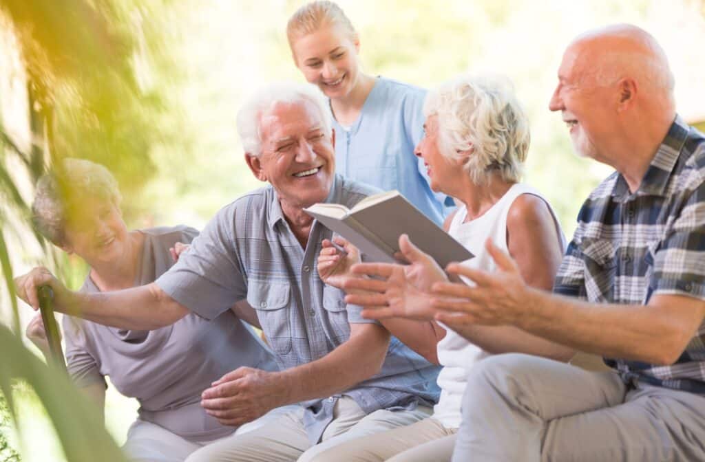 Four older adults enjoy time outdoors in their assisted living community while a caregiver checks in.