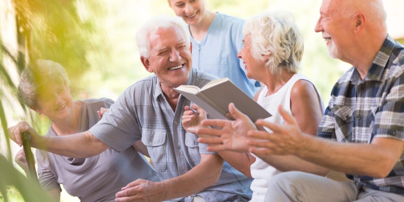 Four older adults enjoy time outdoors in their assisted living community while a caregiver checks in.
