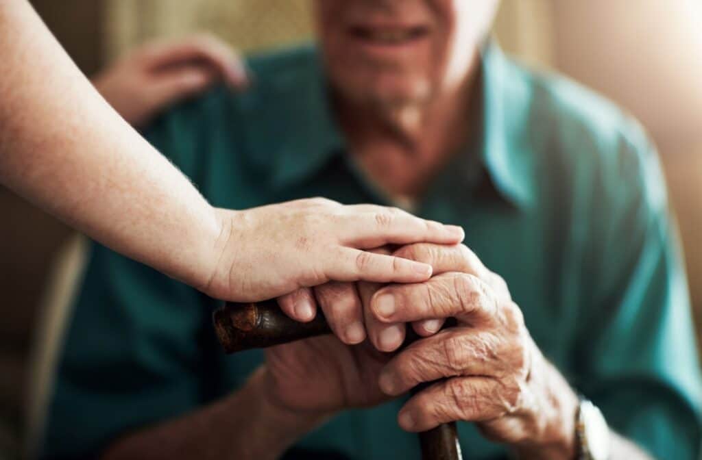 A caretaker places a hand on top of an older adult's hand in an assisted living community.