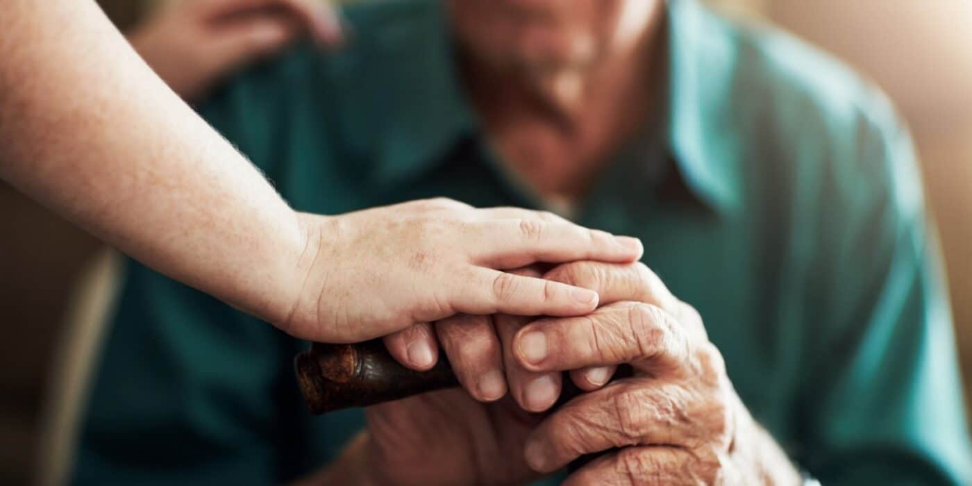 A caretaker places a hand on top of an older adult's hand in an assisted living community.