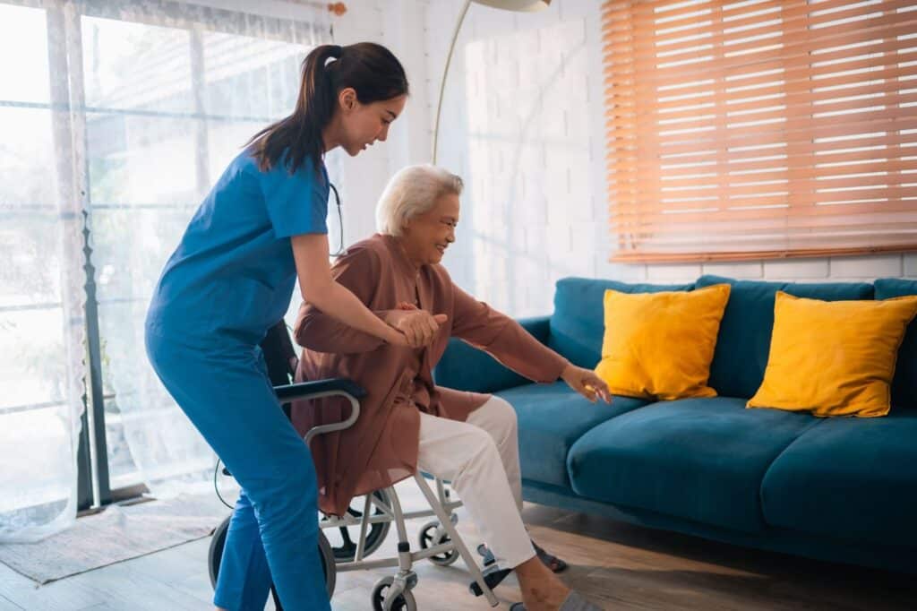 Nurse helping senior off walker onto a couch.