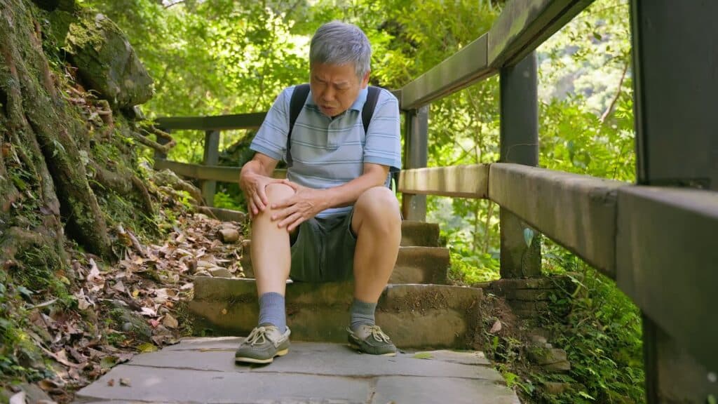 Senior sitting down after hurting their knee on a trail hike.