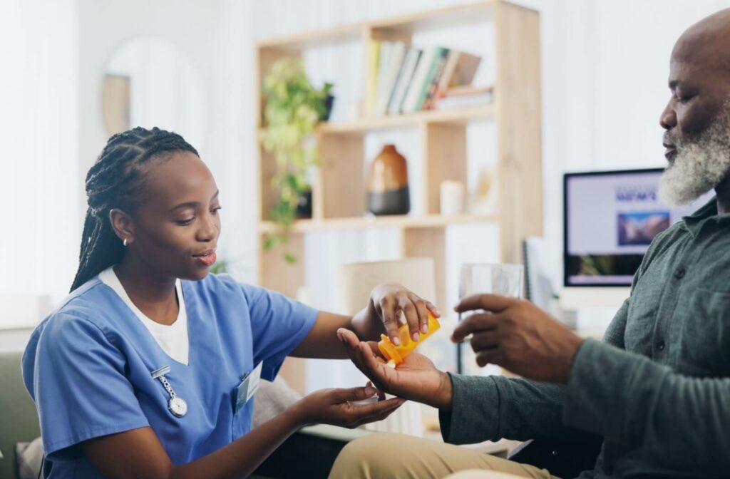 Care staff hands daily medication to older adult in comfortable assisted living apartment with glass of water