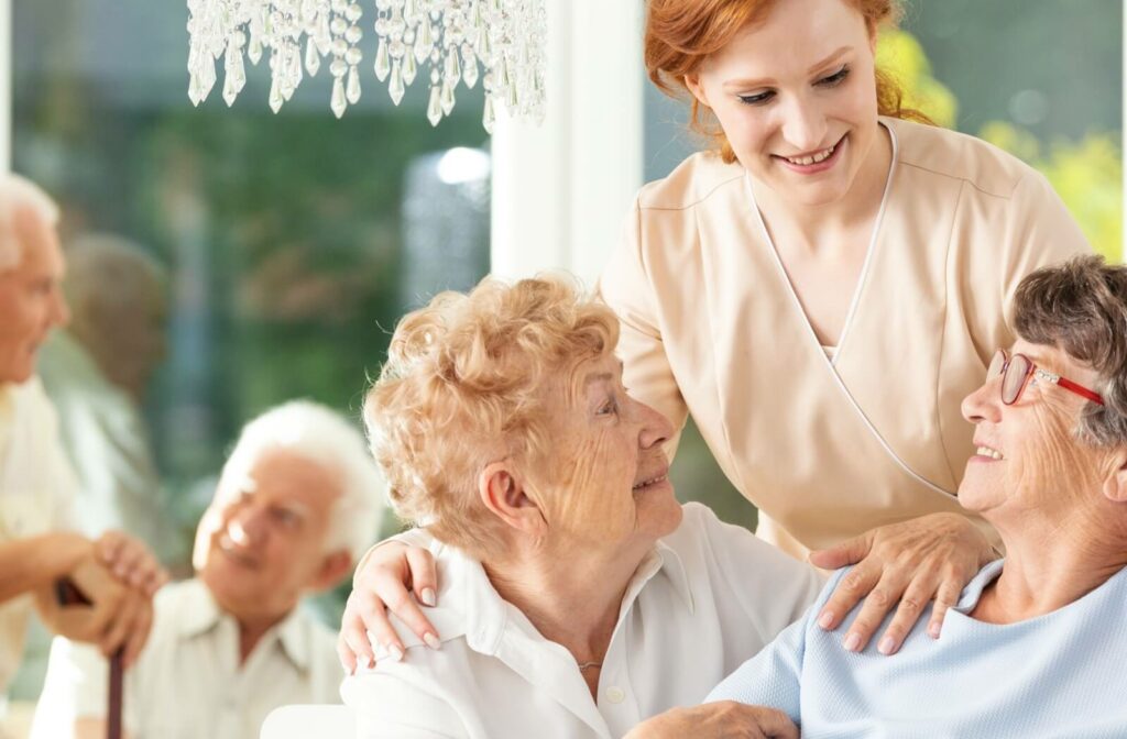 A caregiver talking to 2 senior residents with her arm around their shoulder, sharing smiles and laughter.