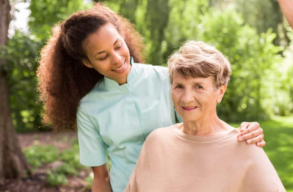 Caregiver supporting older adult outdoors surrounded by greenery