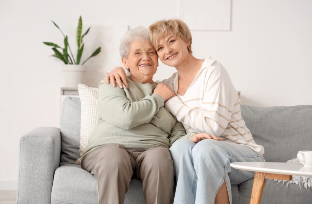 A senior together on a couch smiling in a cozy living room with natural light and houseplant nearby