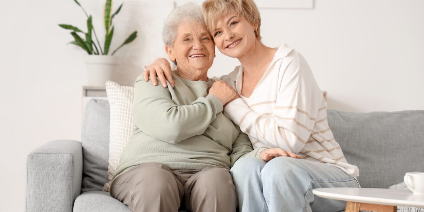 A senior together on a couch smiling in a cozy living room with natural light and houseplant nearby