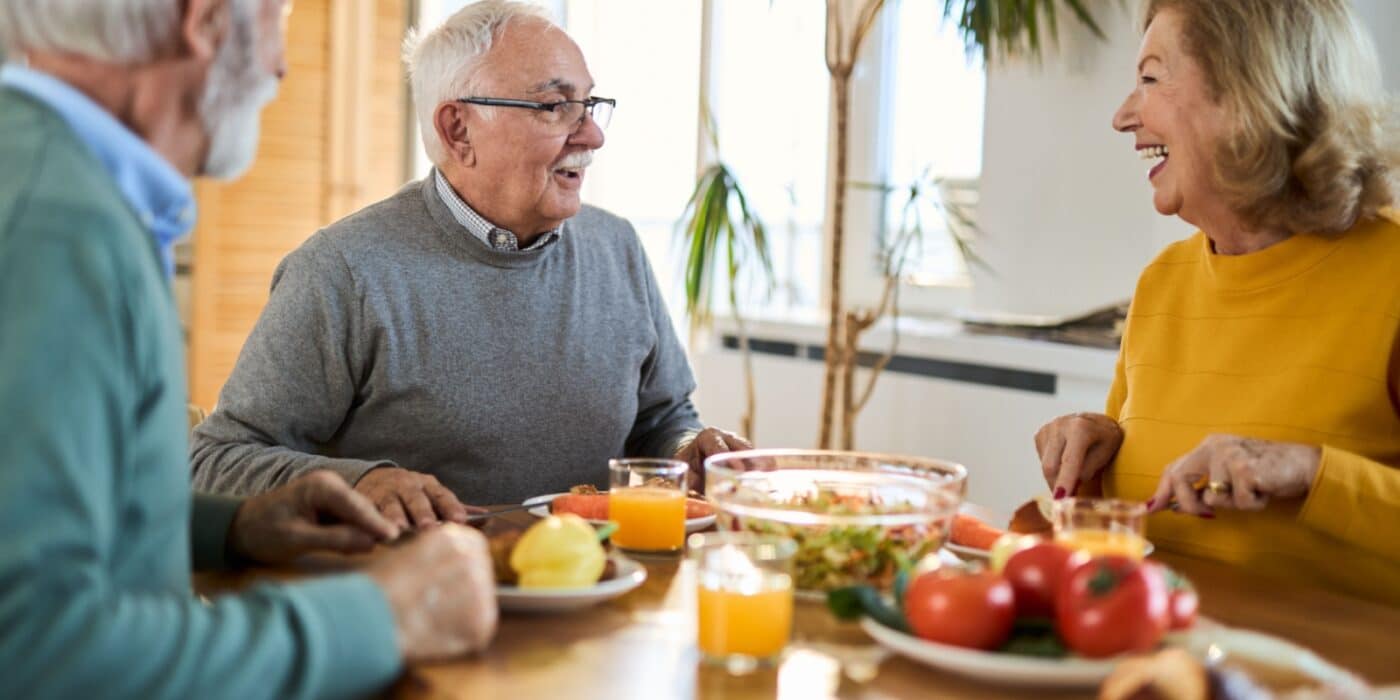 Three seniors laugh over a nutritious meal together in assisted living, enjoying company with like-minded individuals