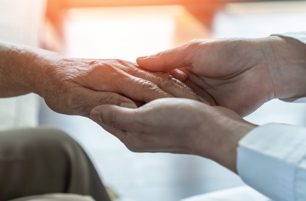 A caregiver takes the hand of an older adult with dementia in front of a sunlit window