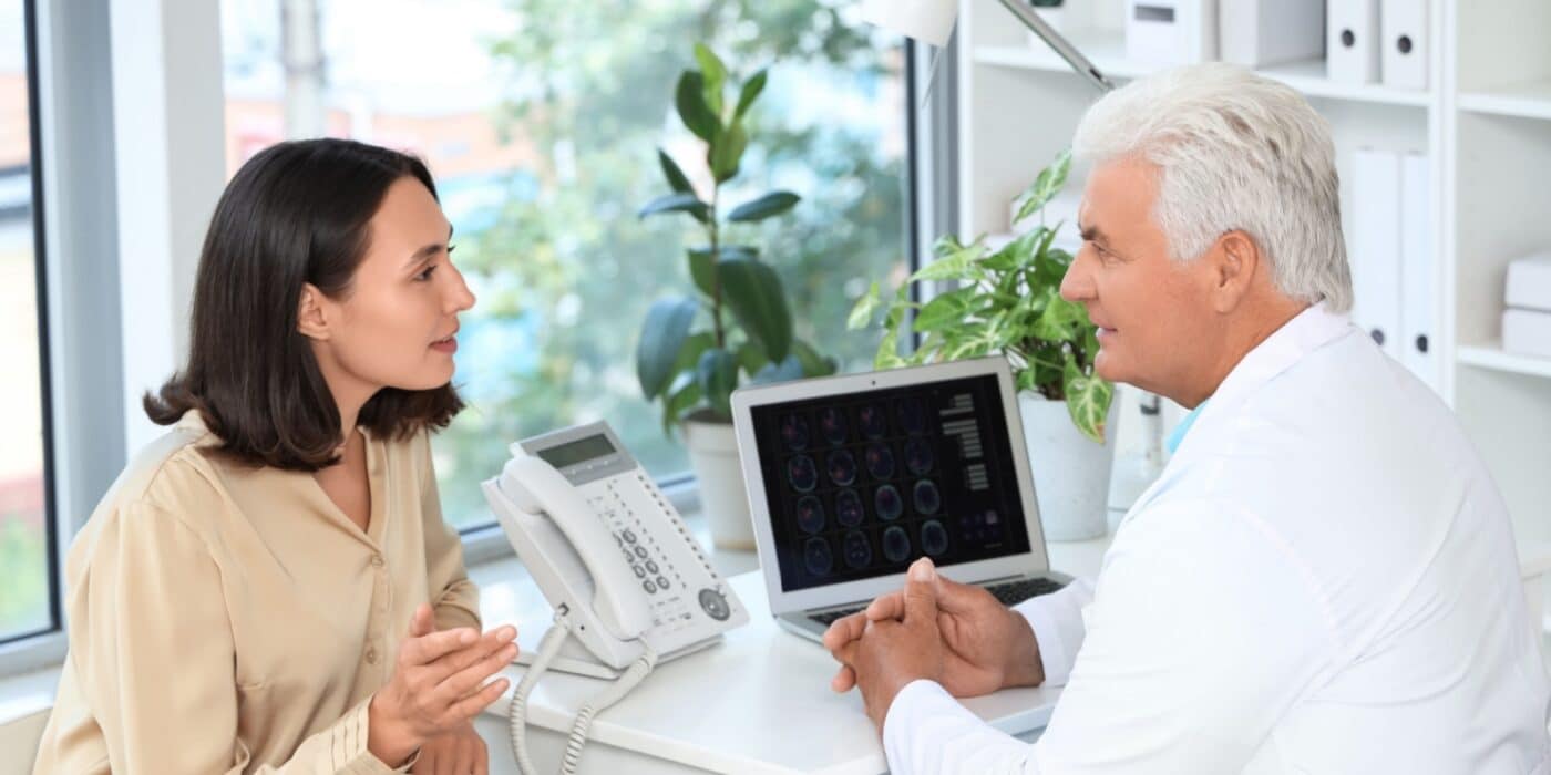 An adult child talks to a neurologist in their well-decorated office after the doctor examined their older parent