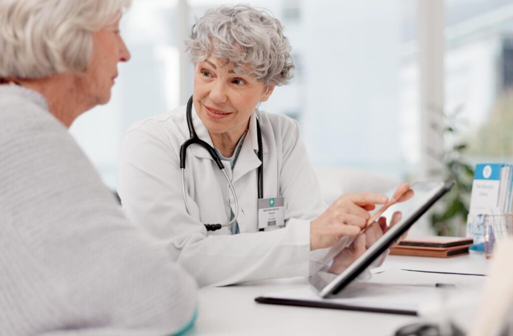 A neurologist gestures to a handheld tablet in their office while showing an older adult the diagnostic results of their latest examination
