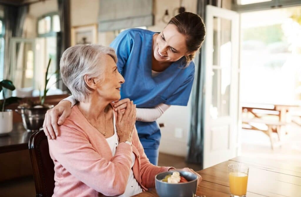 A caregiver checks in on an appreciative resident during breakfast in the lounge of their home in senior living.