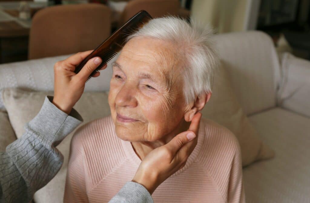 A senior receives help with grooming and brushing their hair as part of one of the ADLs they need assistance with.