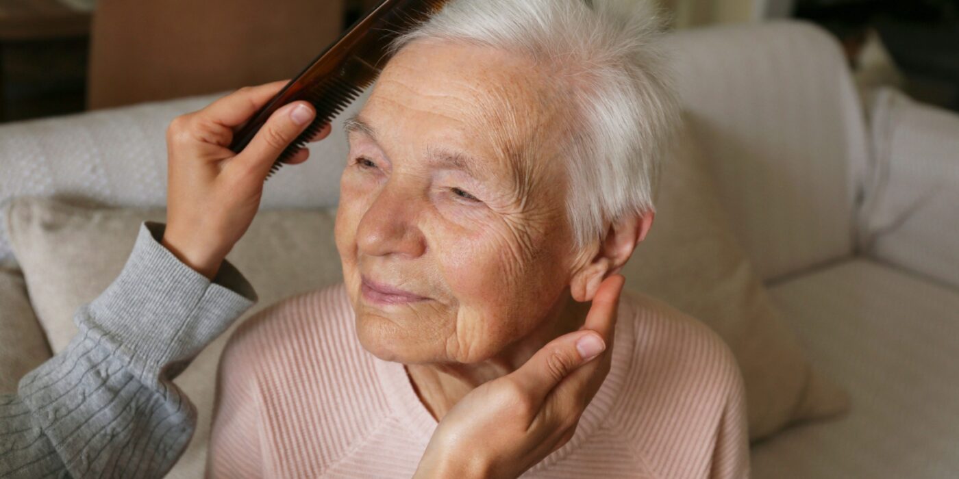 A senior receives help with grooming and brushing their hair as part of one of the ADLs they need assistance with.