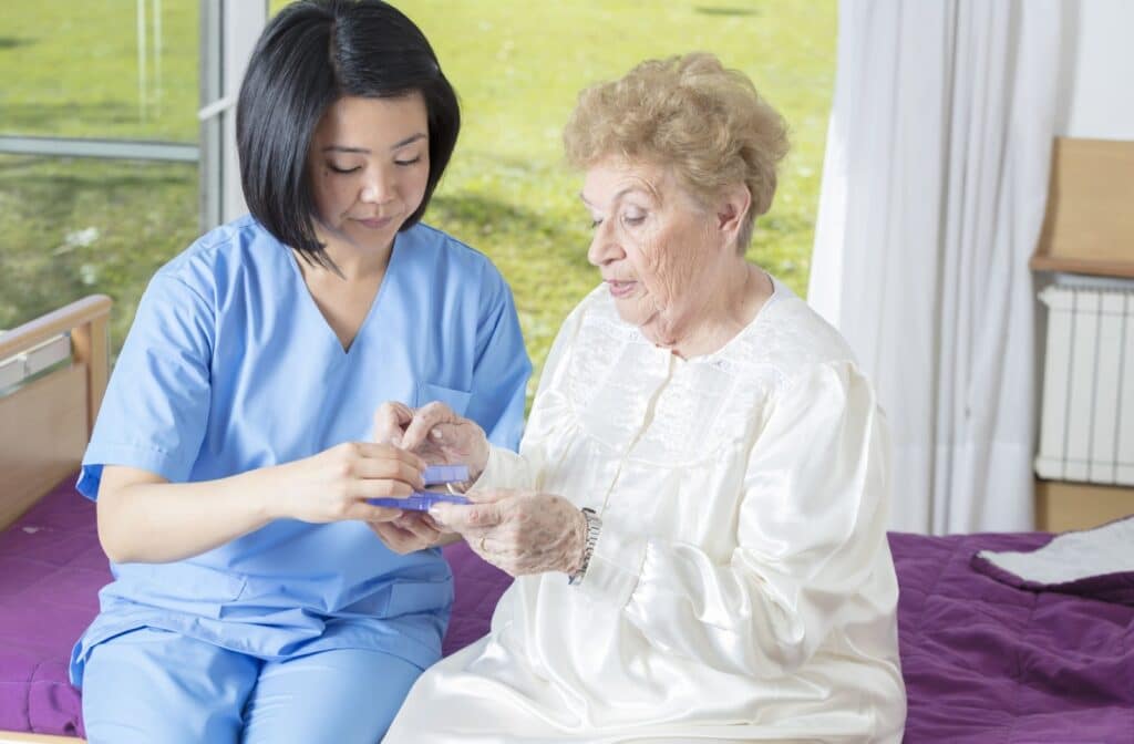A caregiver gives a senior their daily medication from an organized pill box.