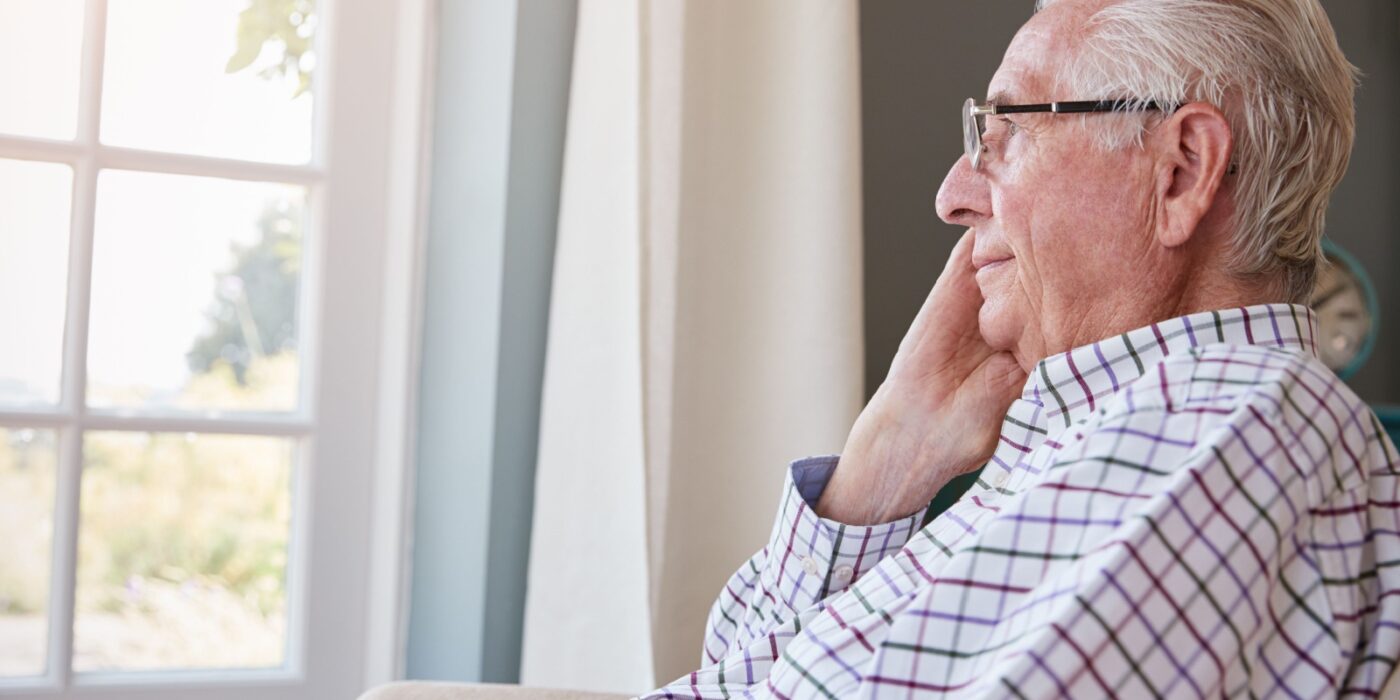 A senior looks out a window, thinking about something nice.