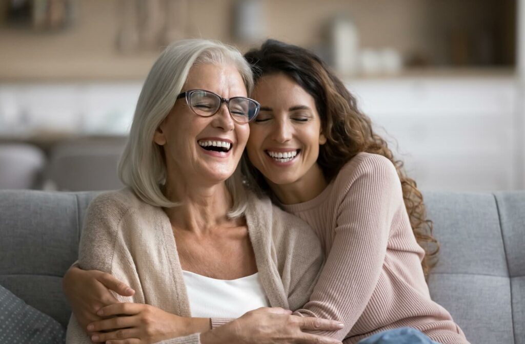 an adult child embraces their senior parent, both smiling warmly in an assisted living apartment.